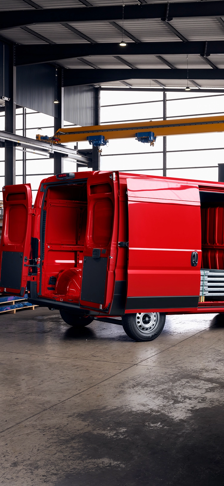 Achteraanzicht schuin van een rode Citroën Jumper met open laadruimte in een magazijn, waarbij grote laadruimte, duurzaamheid en zakelijke veelzijdigheid worden benadrukt.