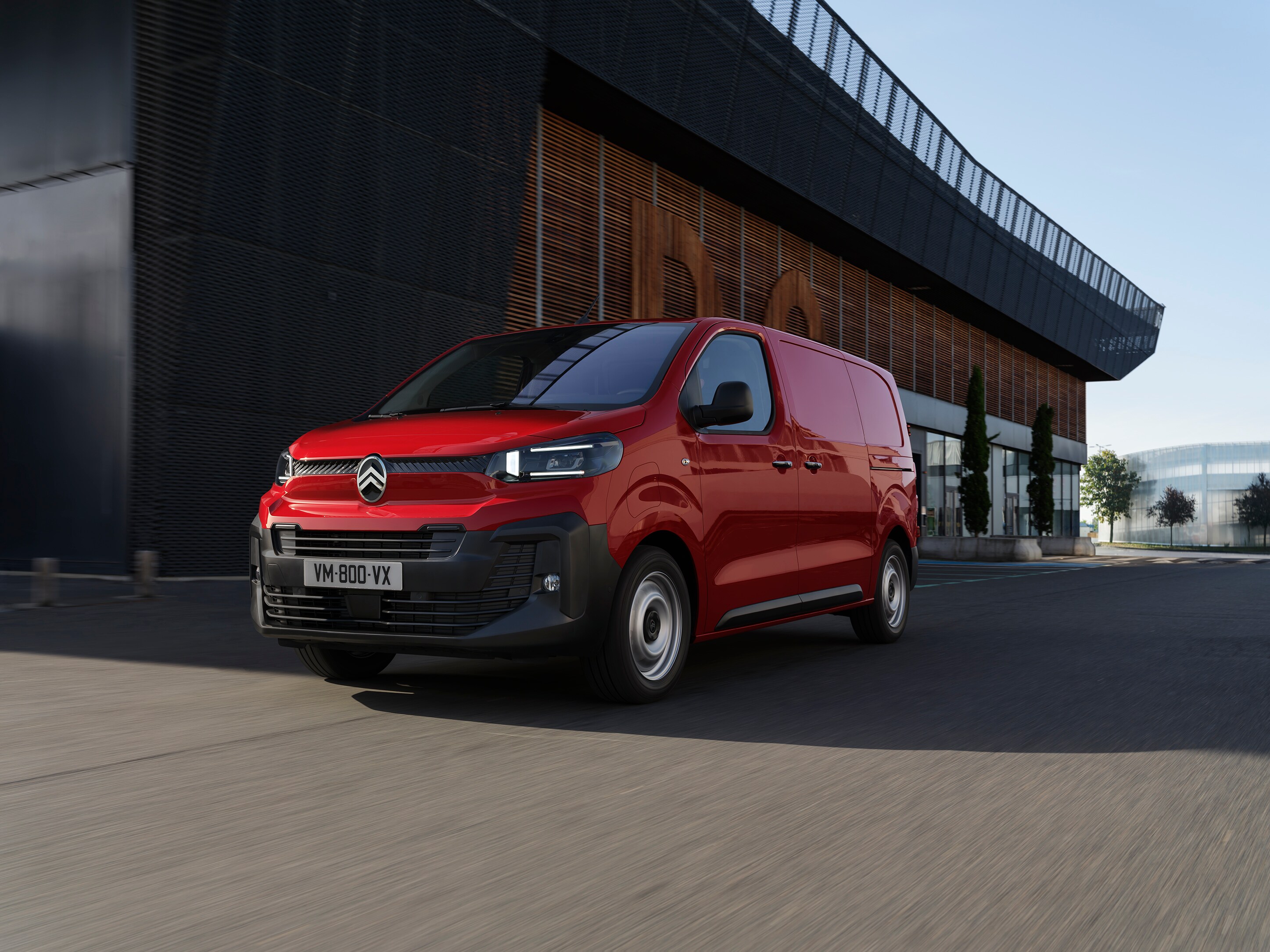 Zijaanzicht van een rode Citroën Jumpy geparkeerd op een open terrein, met strakke proporties, een praktisch design en professionele veelzijdigheid.