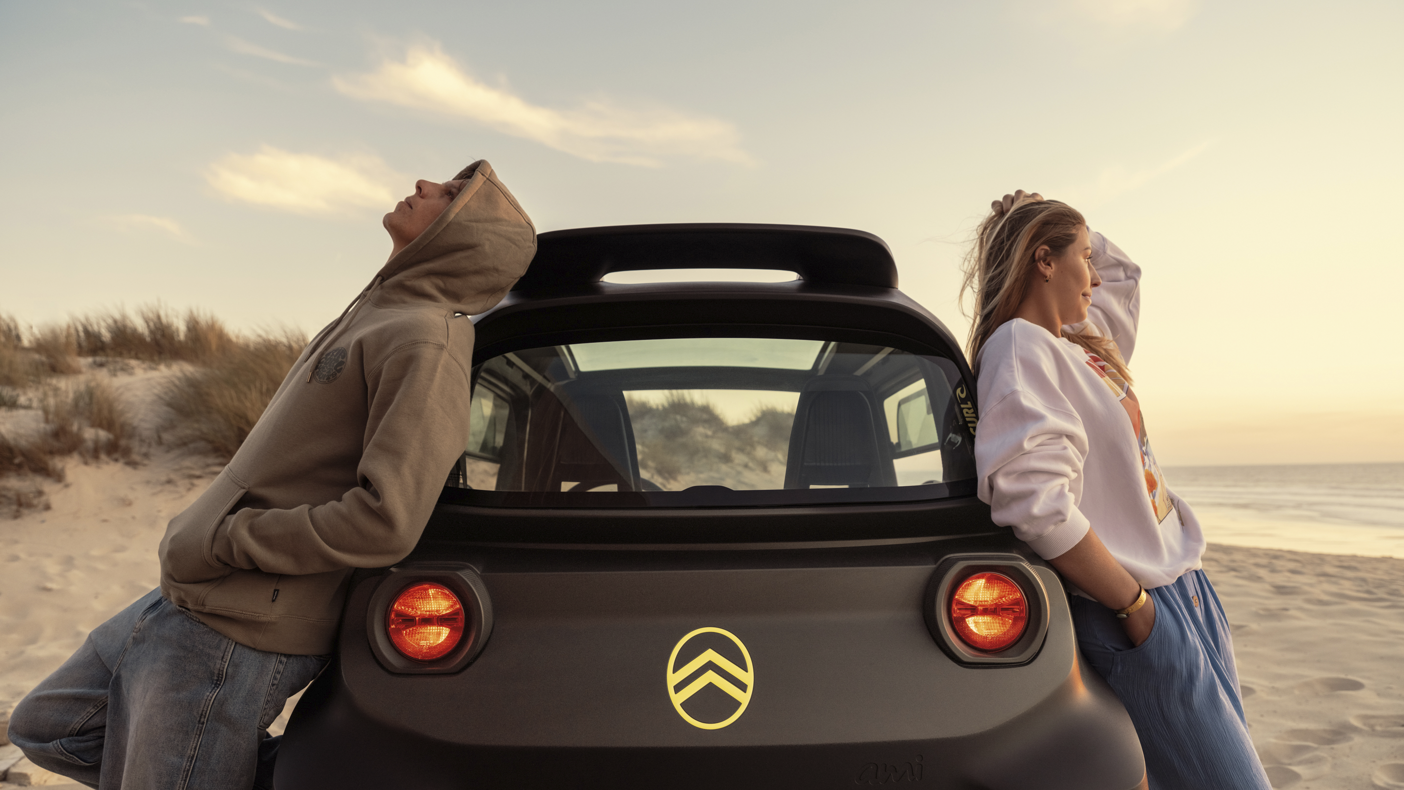 Achteraanzicht bij zonsondergang van de Citroën Ami x Rip Curl, elektrische auto zonder autorijbewijs, met ontspannen vrijheid.