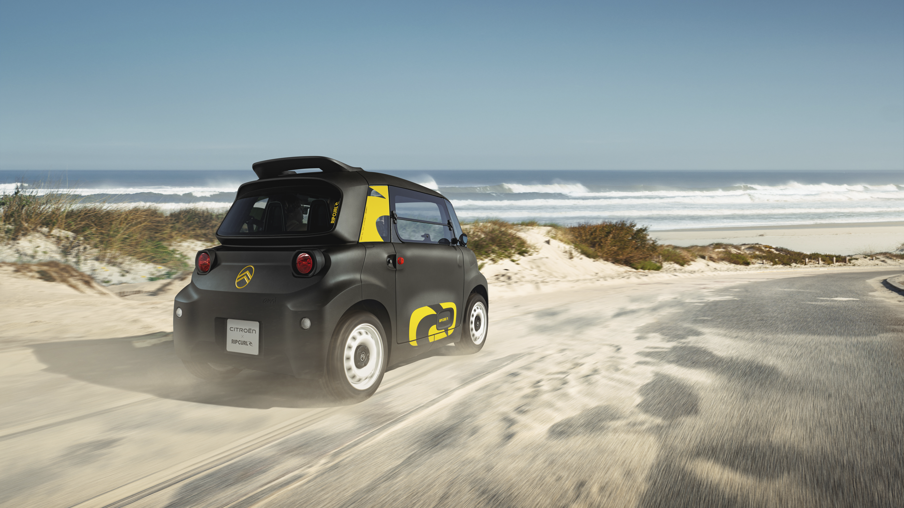 Driekwart achteraanzicht van de Citroën Ami x Rip Curl in actie, elektrische auto zonder autorijbewijs, als illustratie van stedelijke vrijheid.