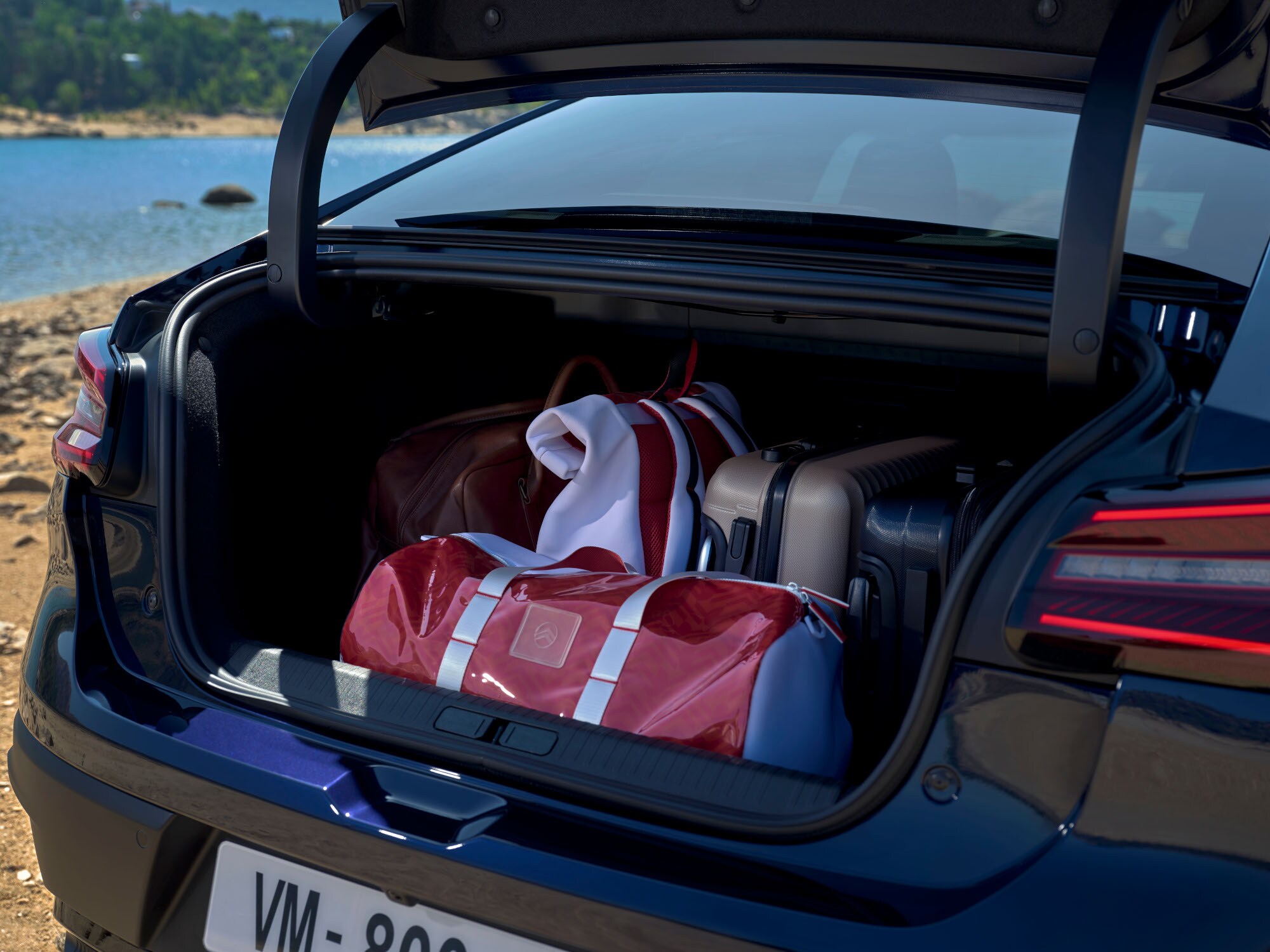 Open bagageruimte van de Citroën ë‑C4 X gevuld met reistassen naast een locatie aan een meer.