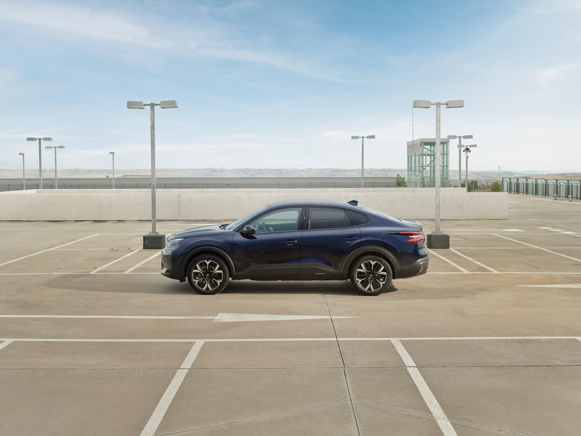 Zijaanzicht van de Citroën ë‑C4 X op een dakterrein met een slank fastback‑profiel voor efficiënte en betaalbare mobiliteit.
